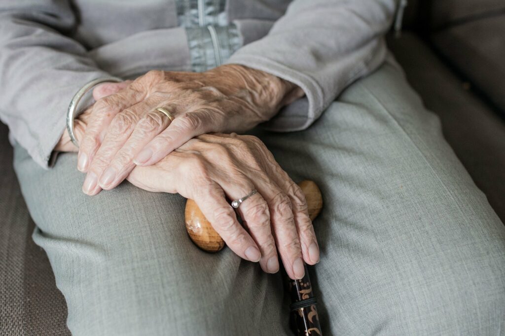 Seniorin sitzt mit Gehstock in der Hand.
