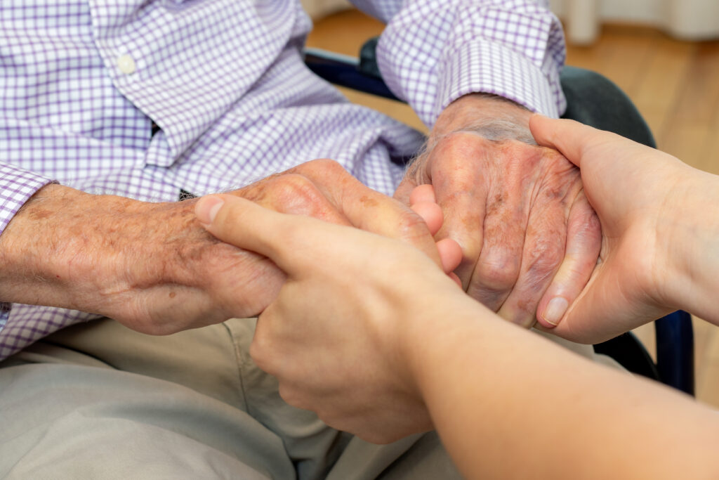 Pfleger hält die Hand eines an Frontotemporaler Demenz erkrankten Patienten.